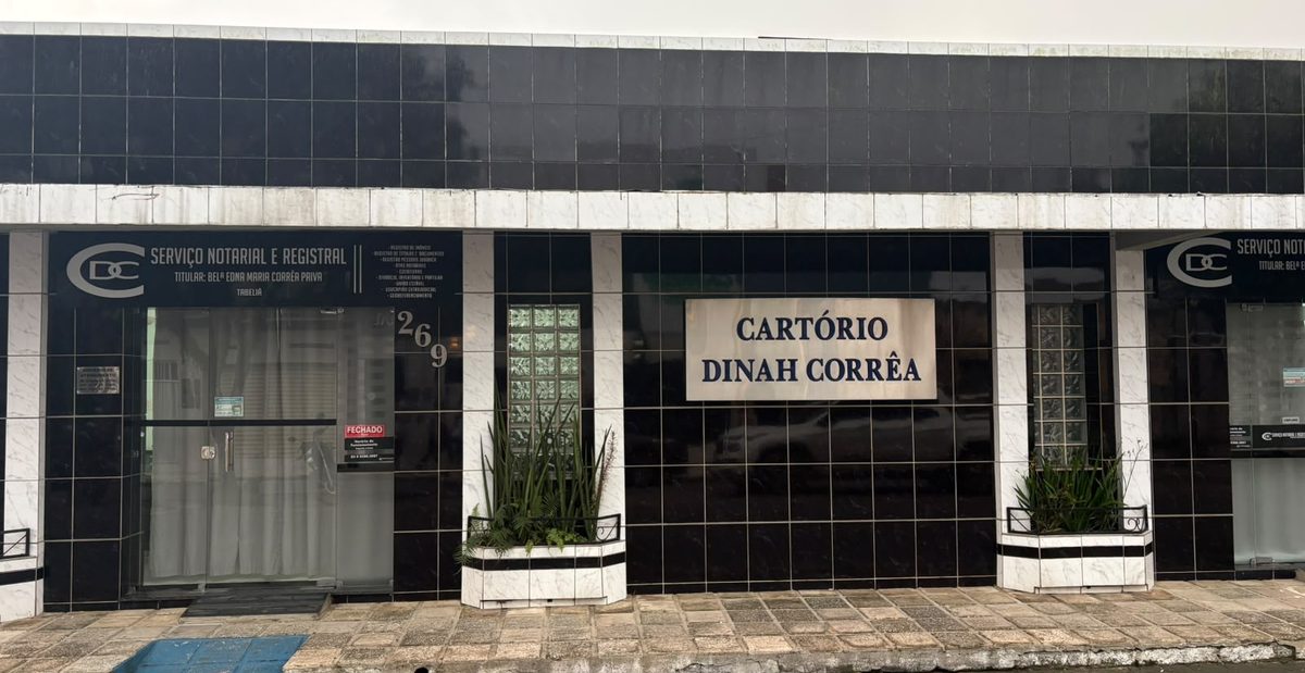 Fachada do Cartório Dinah Corrêa vista da rua durante o dia, prédio de revestimento escuro com a placa do cartório no número 269